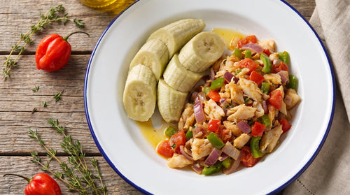 Green banana and saltfish on an enamel plate with peppers, onion, tomato, thyme and scotch bonnets