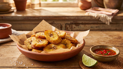Golden fried plantain, bananes pesées, piled in a bowl with a dish of red chilli dipping sauce and a lime wedge